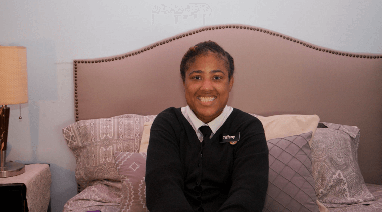 Young black woman wearing a work uniform and sitting on a bed smiling