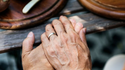 Clasped hands on a wooden table with dishes of food.