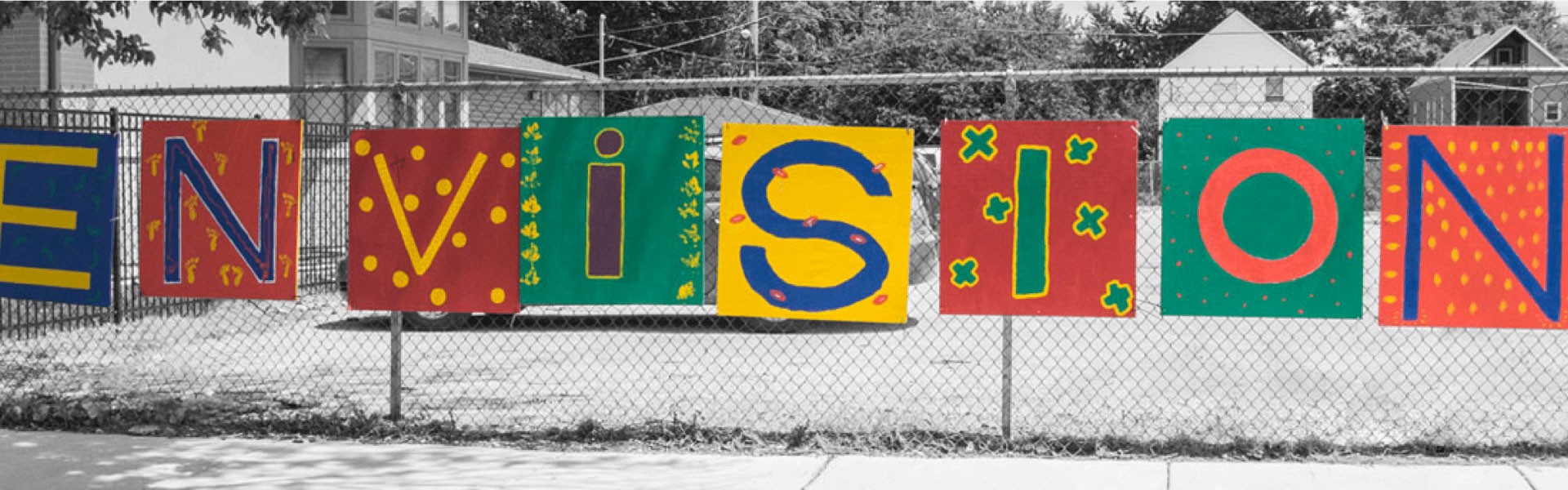 Colorful painted sign saying, "Envision" hanging outside on a fence on a snowy day