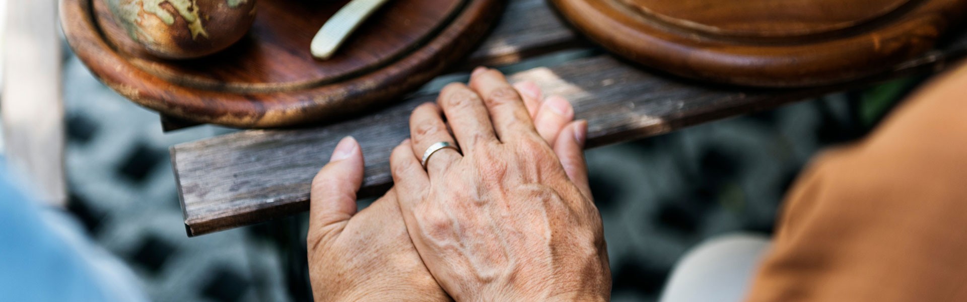 Clasped hands on a wooden table with dishes of food.