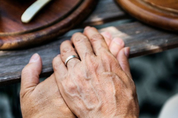 Clasped hands on a wooden table with dishes of food.